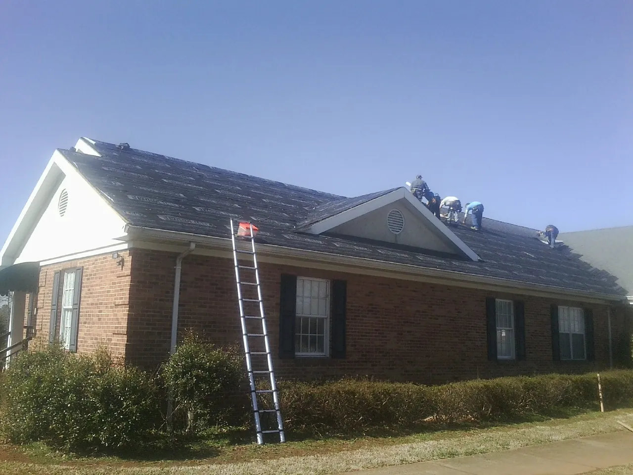 Crew tearing shingles off a brick ranch roof with a ladder set — Emergency Roof Repair work by our crew in San Gabriel
