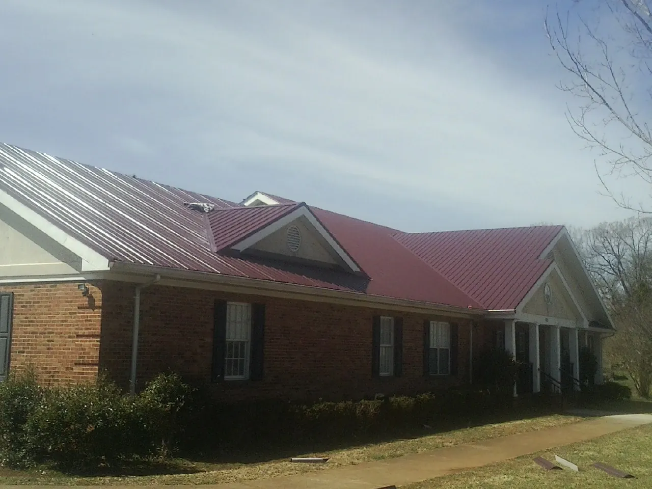 Red metal roof with gabled entries on a long brick building, from a Hail Damage Roof Repair job in San Gabriel