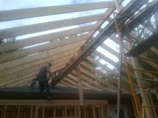 Rafters going up over a new addition with a worker on the wall in San Gabriel
