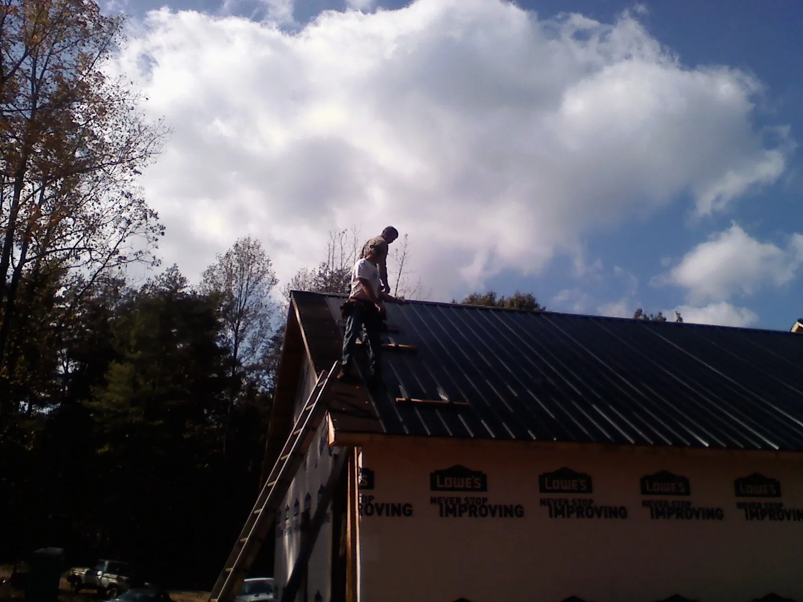 Roofer fastening dark metal panels high against a cloudy sky, from a Roof Inspection job in San Gabriel