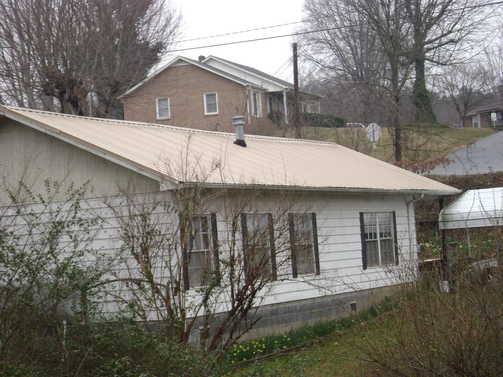 Tan metal roof on a white sided house set into a hillside — Commercial Roofing by Roofing Brothers in San Gabriel